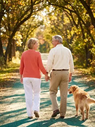 A mature couple walking hand in hand along a sunlit path.