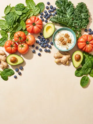 Fresh vegetables, berries and yoghurt arranged on a cream surface.