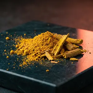 Golden root powder and dried root pieces on a dark stone surface.